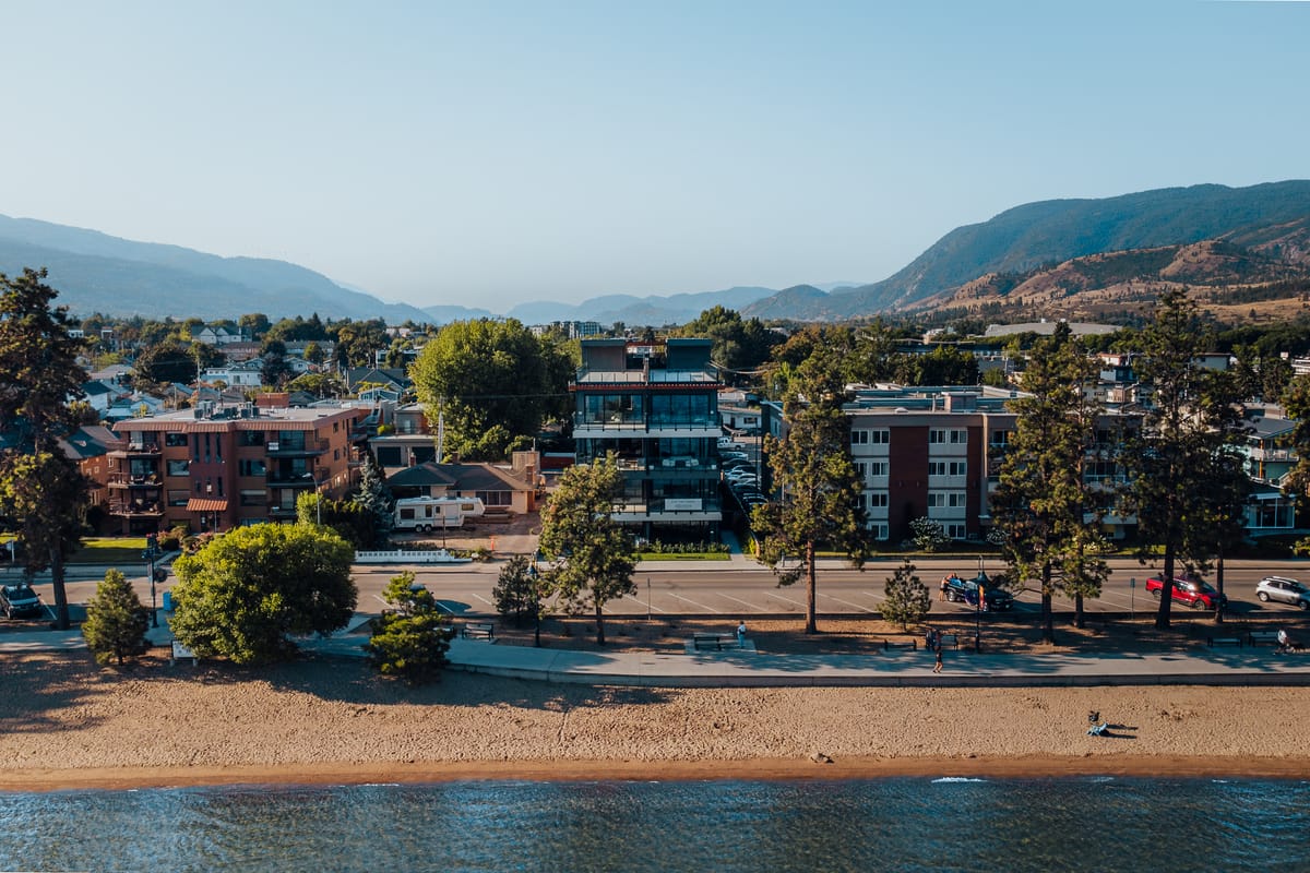 Aerial view of the Penticton beachfront, with Legacy on Lakeshore among the trees and the Okanagan hills in haze behind