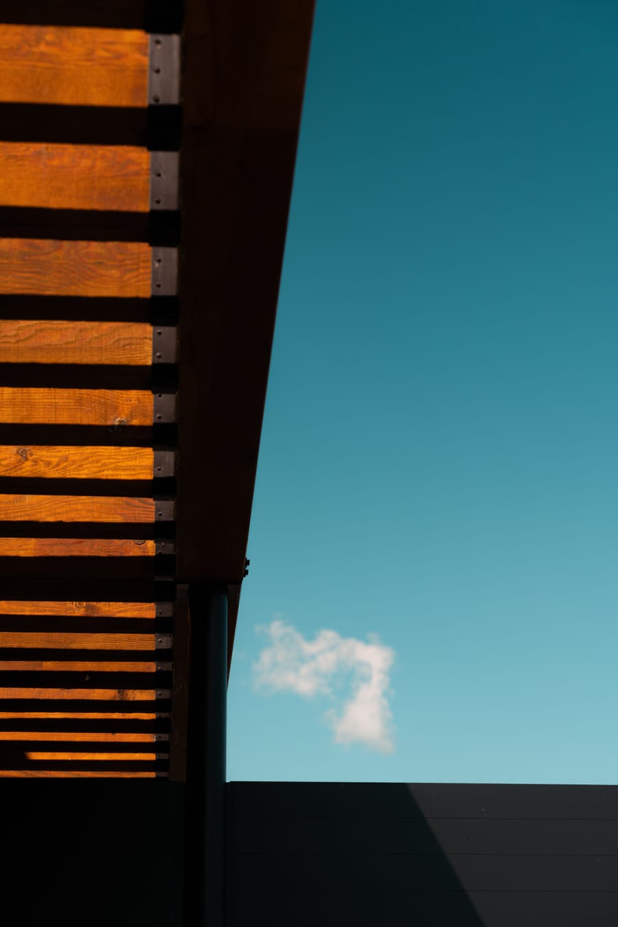 Cedar soffit and steel edge of a rooftop canopy against a clear sky