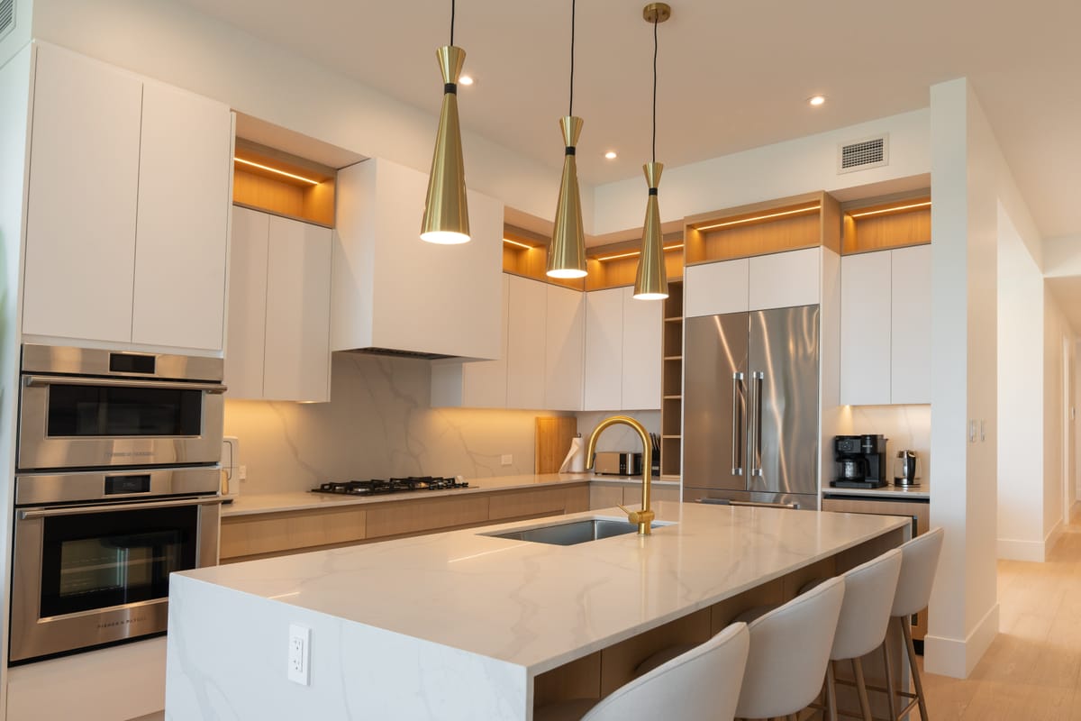 Kitchen at Legacy on Lakeshore: quartz island, brass tap and three brass pendants under lit upper cabinets