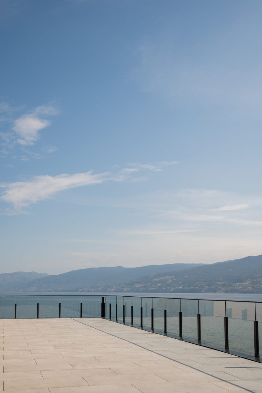 Pale paving and a glass rail at the terrace edge with the lake and hills beyond